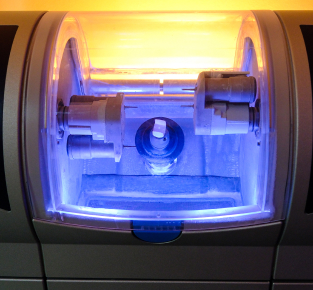 Ultrasonic dental cleaner device with glowing blue interior and warm yellow overhead lighting.