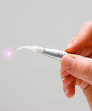 Hand holding dental laser tool emitting pink light against gray background.