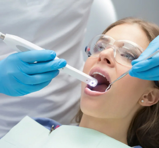 Dentist in protective gloves and eyewear examining patient's mouth during dental procedure in clinical setting.