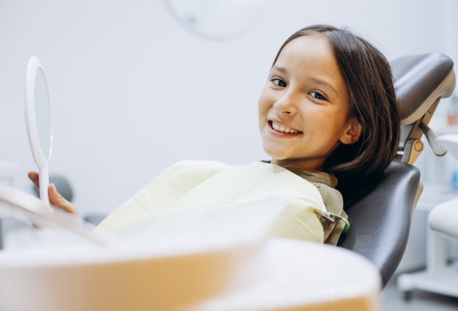 Young girl smiling in dental chair during routine checkup at modern dentist office.
