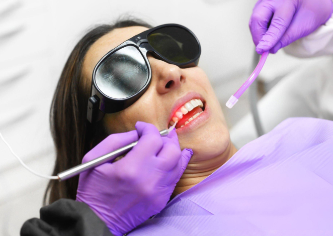 Dentist in purple gloves examining patient's teeth with magnifying loupes in clinical setting.
