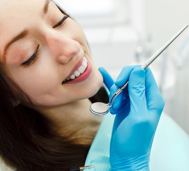 Woman receiving dental examination from dentist wearing blue gloves in clinical setting.