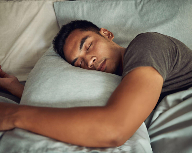 Man sleeping peacefully on pillow in bed, demonstrating restful sleep related to dental health.