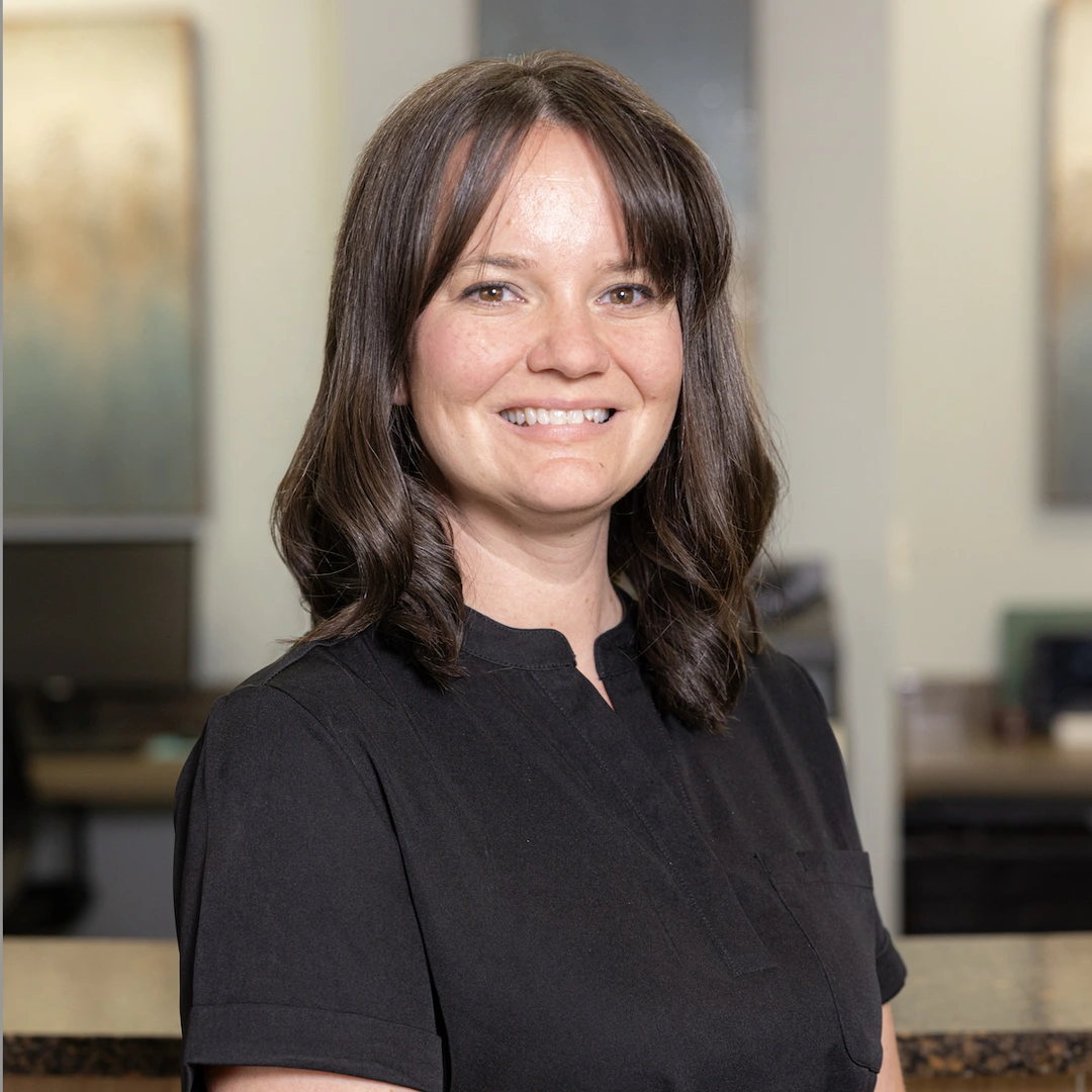Professional woman smiling at camera in modern dental office setting, wearing black shirt.