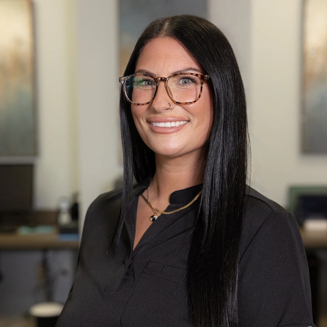Professional woman with glasses smiling in modern dental office setting, wearing black shirt.