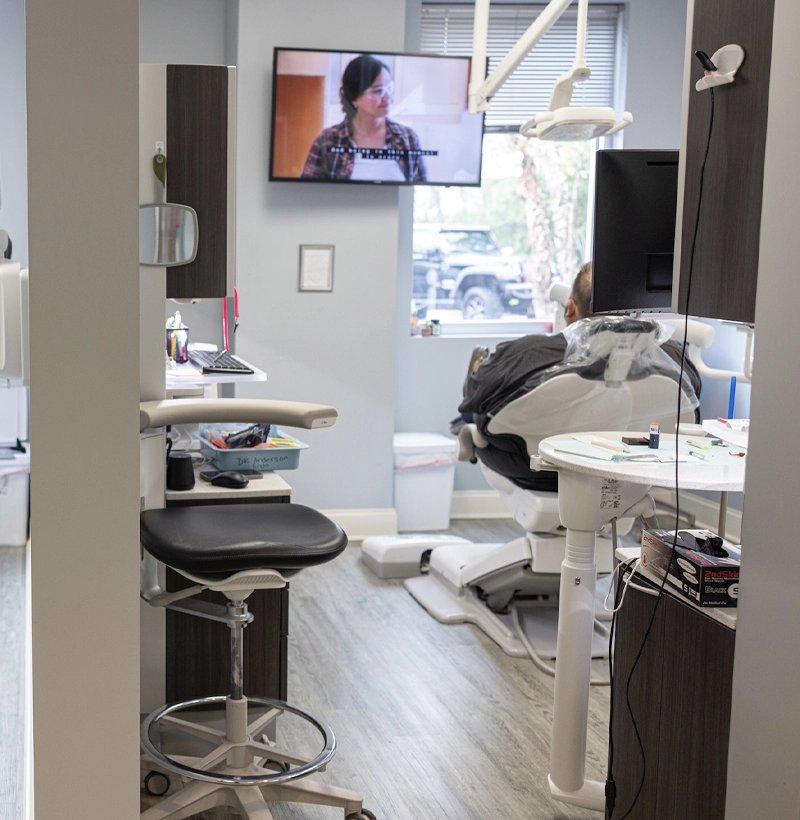 Modern dental operatory with chair, equipment, monitor displaying patient information, and bright clinical workspace.
