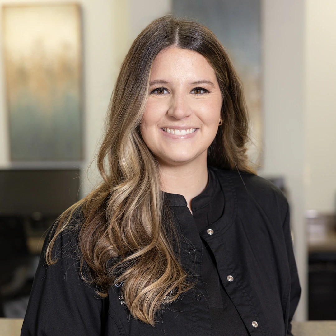 Professional woman smiling in black blazer, modern office setting, dental practice environment.