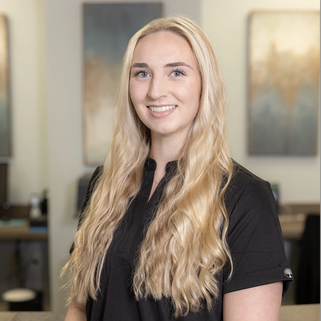 Professional woman with blonde hair smiling in modern dental office interior setting.