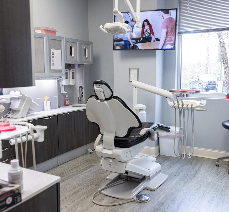 Modern dental operatory with empty chair, overhead light, and mounted monitor displaying patient information.