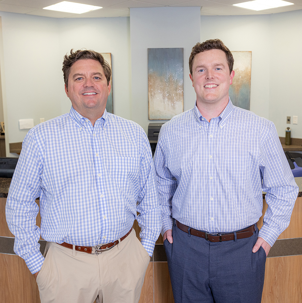 Two men in blue checkered shirts standing in a modern dental office interior.